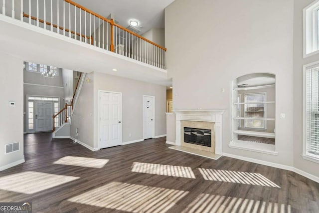 unfurnished living room featuring a towering ceiling, plenty of natural light, and dark hardwood / wood-style flooring