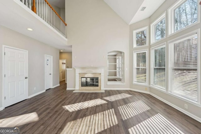 unfurnished living room with high vaulted ceiling, dark hardwood / wood-style flooring, a premium fireplace, and a healthy amount of sunlight