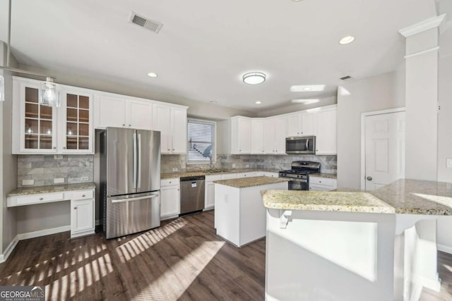 kitchen with appliances with stainless steel finishes, white cabinetry, light stone countertops, a kitchen island, and a breakfast bar area