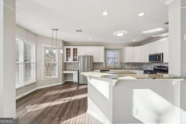 kitchen with a wealth of natural light, pendant lighting, white cabinets, stainless steel appliances, and light stone counters