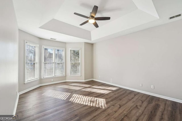 empty room with ceiling fan, dark wood-type flooring, and a tray ceiling