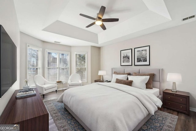 bedroom featuring ceiling fan, multiple windows, a tray ceiling, and dark hardwood / wood-style flooring