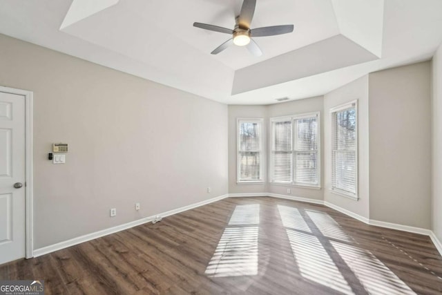 empty room with ceiling fan, dark hardwood / wood-style floors, and a tray ceiling