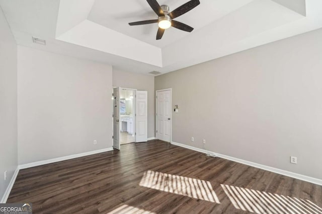 empty room with ceiling fan, dark hardwood / wood-style flooring, and a tray ceiling