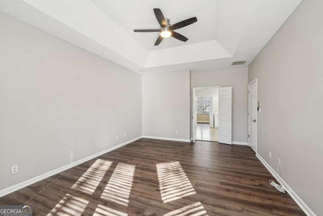 unfurnished bedroom with ceiling fan, a tray ceiling, and dark hardwood / wood-style flooring