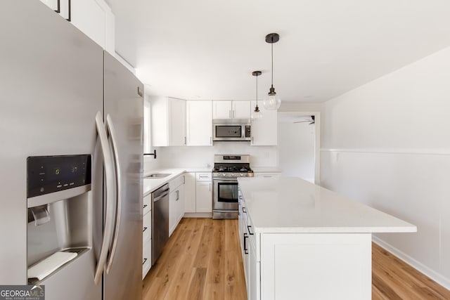 kitchen with pendant lighting, appliances with stainless steel finishes, light wood-type flooring, white cabinetry, and a kitchen island