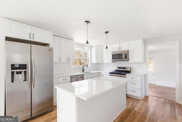 kitchen featuring decorative light fixtures, light wood-type flooring, white cabinetry, a center island, and stainless steel appliances