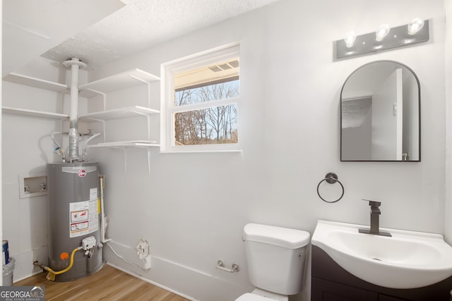 bathroom with toilet, hardwood / wood-style floors, a textured ceiling, vanity, and water heater