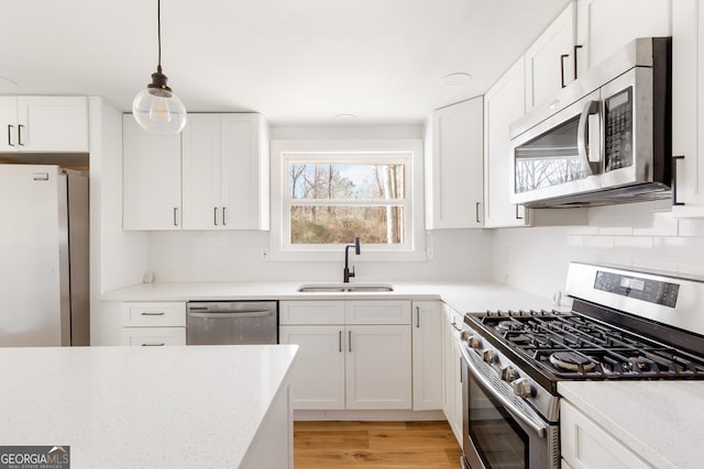 kitchen featuring pendant lighting, white cabinets, stainless steel appliances, sink, and backsplash