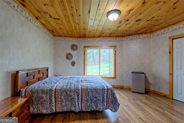 bedroom featuring hardwood / wood-style flooring, wooden ceiling, and stainless steel refrigerator