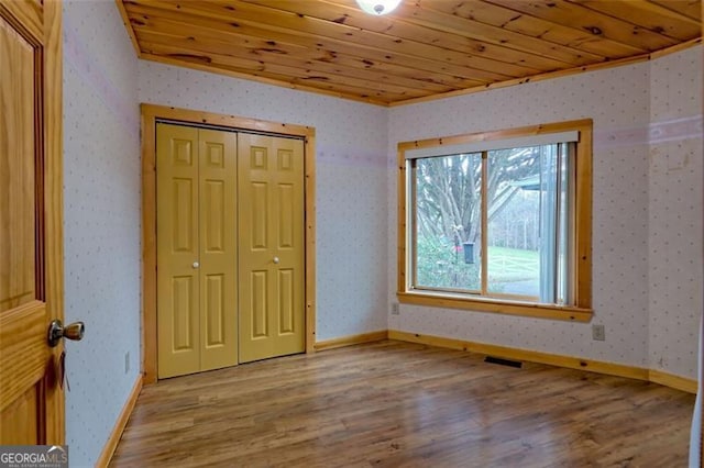 unfurnished bedroom featuring ornamental molding, light hardwood / wood-style flooring, wooden ceiling, and a closet