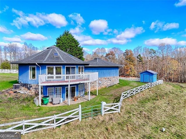 rear view of property with a storage shed, a lawn, central AC, a wooden deck, and a patio area