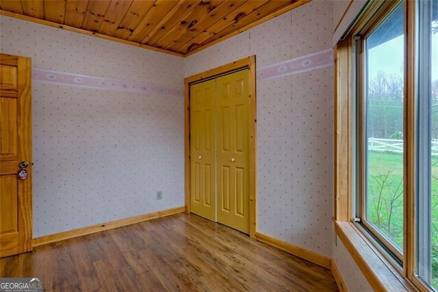 unfurnished bedroom featuring hardwood / wood-style floors, wood ceiling, ornamental molding, and a closet