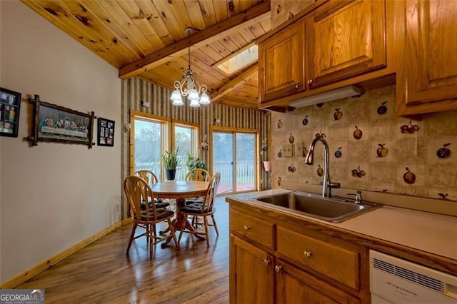 kitchen with pendant lighting, vaulted ceiling with skylight, dishwasher, sink, and light hardwood / wood-style flooring