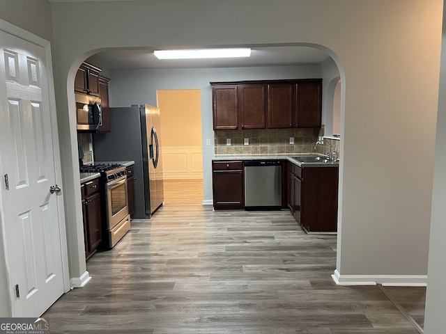 kitchen with light hardwood / wood-style flooring, appliances with stainless steel finishes, sink, backsplash, and dark brown cabinetry