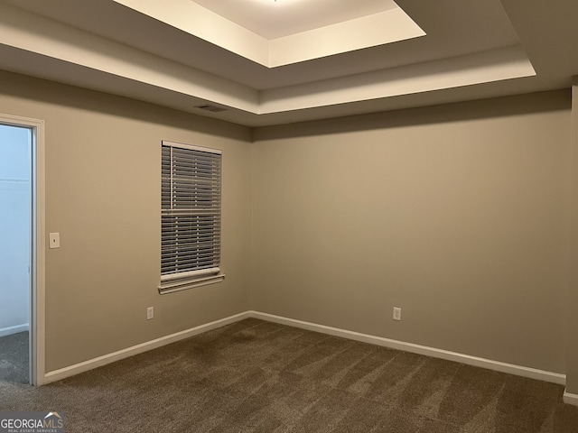 spare room featuring dark colored carpet and a tray ceiling