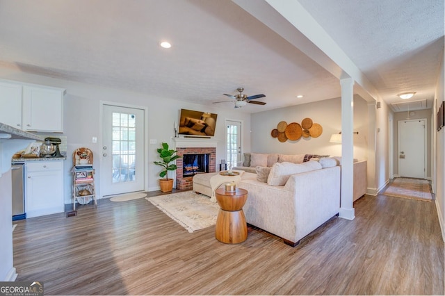 living room featuring ceiling fan, wood-type flooring, a textured ceiling, and a fireplace