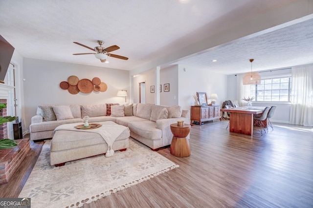 living room featuring ceiling fan, a textured ceiling, dark hardwood / wood-style floors, and a brick fireplace