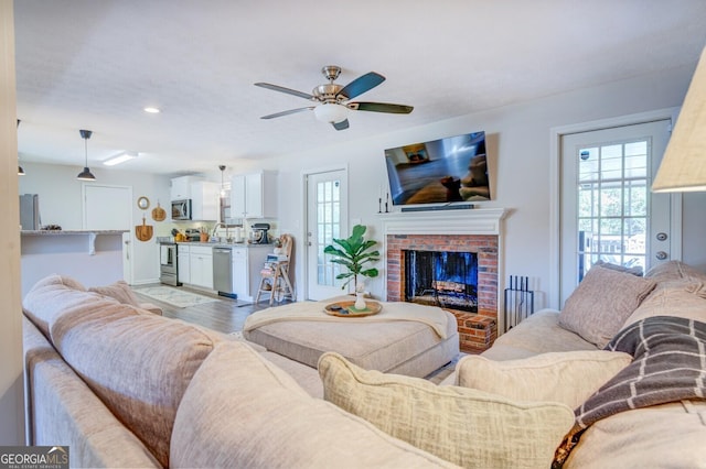 living room with ceiling fan, sink, light hardwood / wood-style floors, and a fireplace