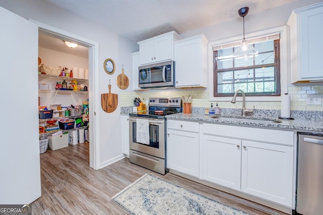 kitchen with light stone countertops, white cabinetry, stainless steel appliances, sink, and light hardwood / wood-style flooring