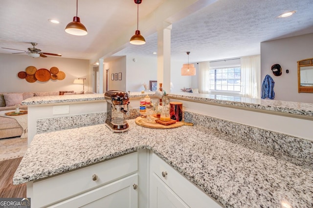 kitchen with kitchen peninsula, hanging light fixtures, white cabinets, light stone counters, and a textured ceiling