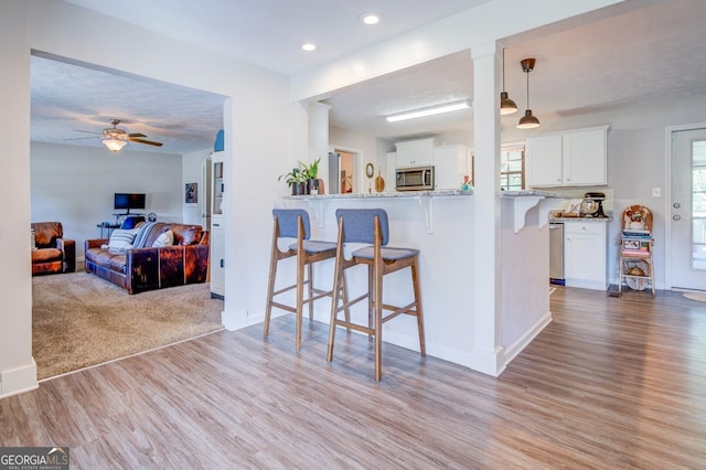 kitchen featuring appliances with stainless steel finishes, hanging light fixtures, white cabinets, kitchen peninsula, and a breakfast bar