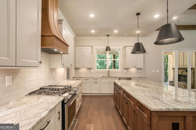 kitchen featuring light stone countertops, white cabinets, custom exhaust hood, decorative light fixtures, and high end stainless steel range oven