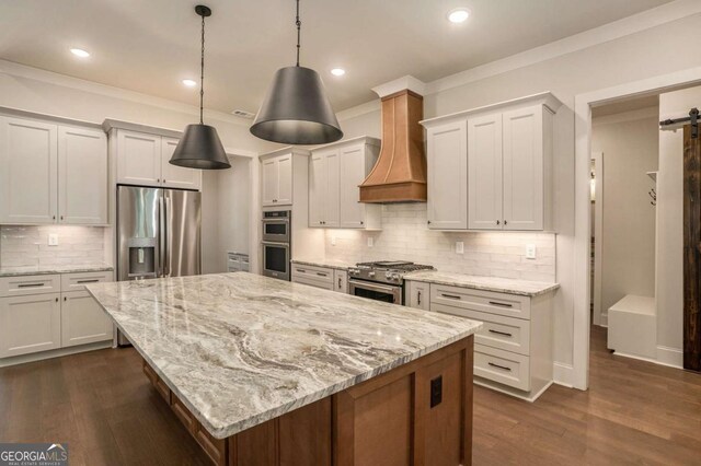 kitchen featuring decorative light fixtures, white cabinetry, stainless steel appliances, premium range hood, and a barn door