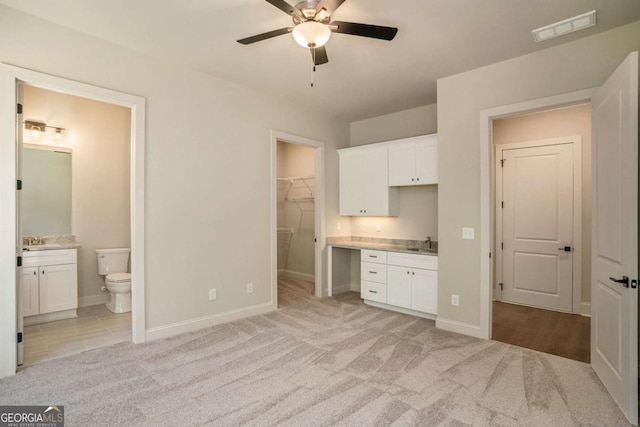 unfurnished bedroom featuring visible vents, ensuite bath, built in desk, light carpet, and a walk in closet