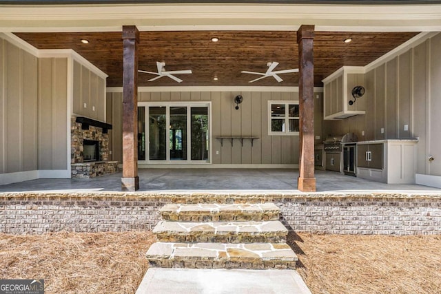 view of exterior entry with exterior kitchen, an outdoor stone fireplace, ceiling fan, and a patio