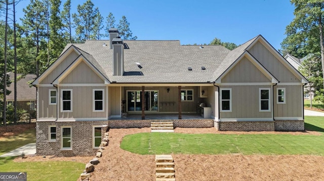 rear view of house with a yard, brick siding, a chimney, and a shingled roof