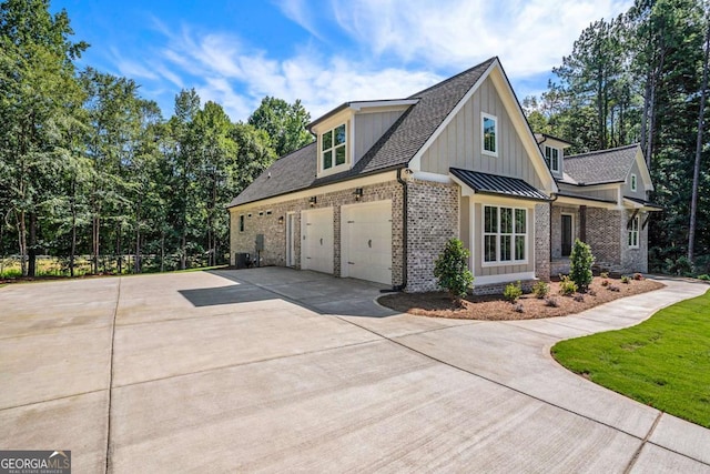 view of side of home with brick siding, board and batten siding, a shingled roof, concrete driveway, and a standing seam roof