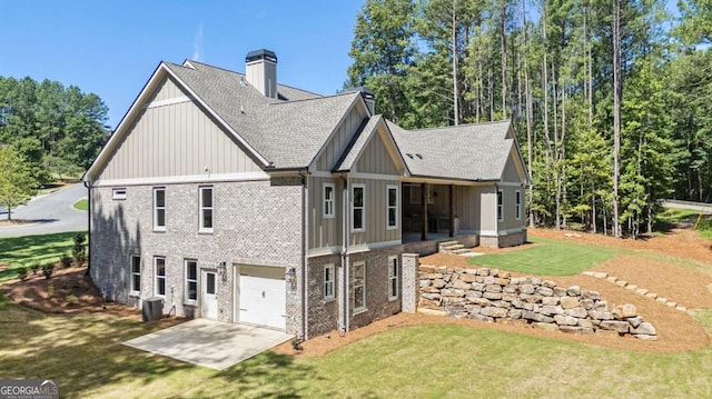 rear view of house with brick siding, a chimney, concrete driveway, a lawn, and board and batten siding