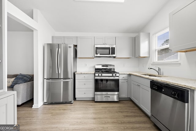 kitchen with sink, light hardwood / wood-style flooring, gray cabinets, appliances with stainless steel finishes, and vaulted ceiling