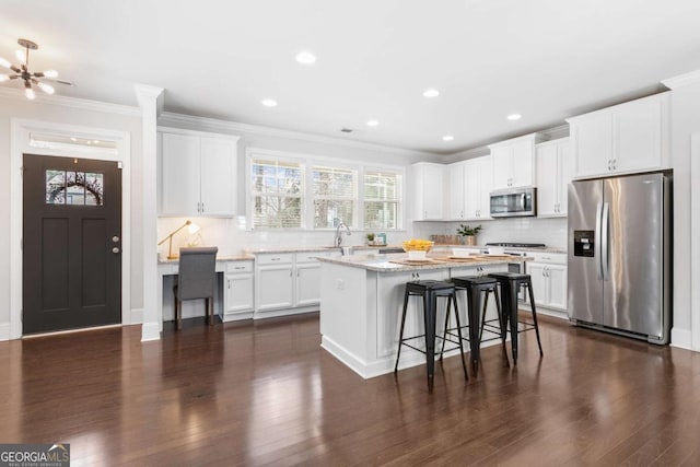 kitchen with appliances with stainless steel finishes, white cabinetry, light stone counters, a kitchen bar, and a kitchen island