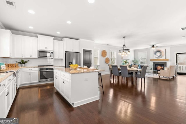 kitchen featuring light stone countertops, white cabinets, a kitchen island, stainless steel appliances, and hanging light fixtures