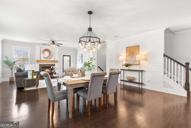 dining room featuring a fireplace, dark hardwood / wood-style flooring, ceiling fan with notable chandelier, and ornamental molding