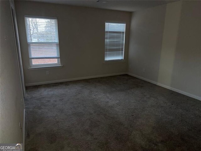 spare room with dark colored carpet and plenty of natural light