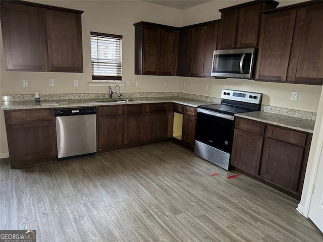 kitchen featuring light stone countertops, appliances with stainless steel finishes, sink, light wood-type flooring, and dark brown cabinetry