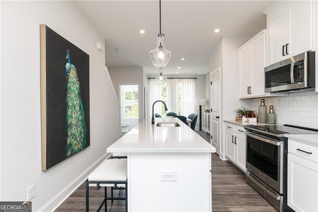 kitchen with stainless steel appliances, a sink, white cabinetry, decorative backsplash, and an island with sink