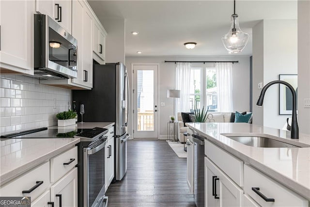 kitchen featuring stainless steel appliances, a sink, white cabinetry, hanging light fixtures, and backsplash