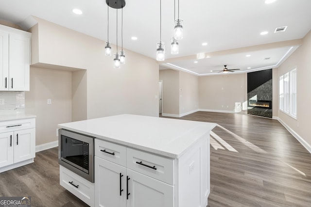 kitchen with pendant lighting, white cabinets, a high end fireplace, dark wood-type flooring, and stainless steel microwave