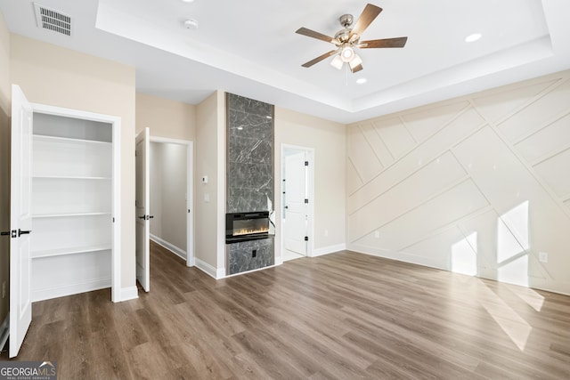 unfurnished living room featuring ceiling fan, hardwood / wood-style floors, a tray ceiling, and a high end fireplace