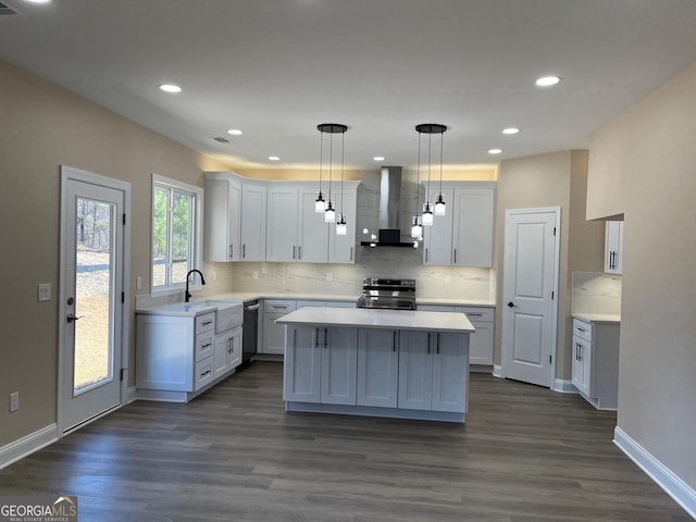 kitchen with appliances with stainless steel finishes, white cabinetry, decorative light fixtures, a kitchen island, and wall chimney exhaust hood