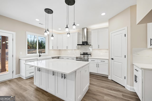 kitchen with a center island, decorative light fixtures, white cabinetry, wall chimney range hood, and stainless steel appliances