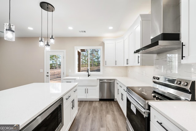 kitchen with wall chimney range hood, white cabinetry, appliances with stainless steel finishes, and decorative backsplash