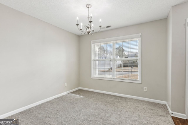 spare room featuring an inviting chandelier, carpet floors, and a textured ceiling