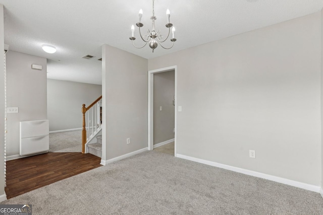 empty room featuring carpet, a textured ceiling, and an inviting chandelier