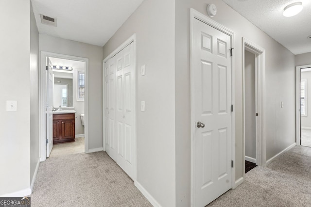 corridor featuring plenty of natural light, sink, light carpet, and a textured ceiling