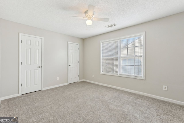 spare room with a textured ceiling, light colored carpet, and ceiling fan